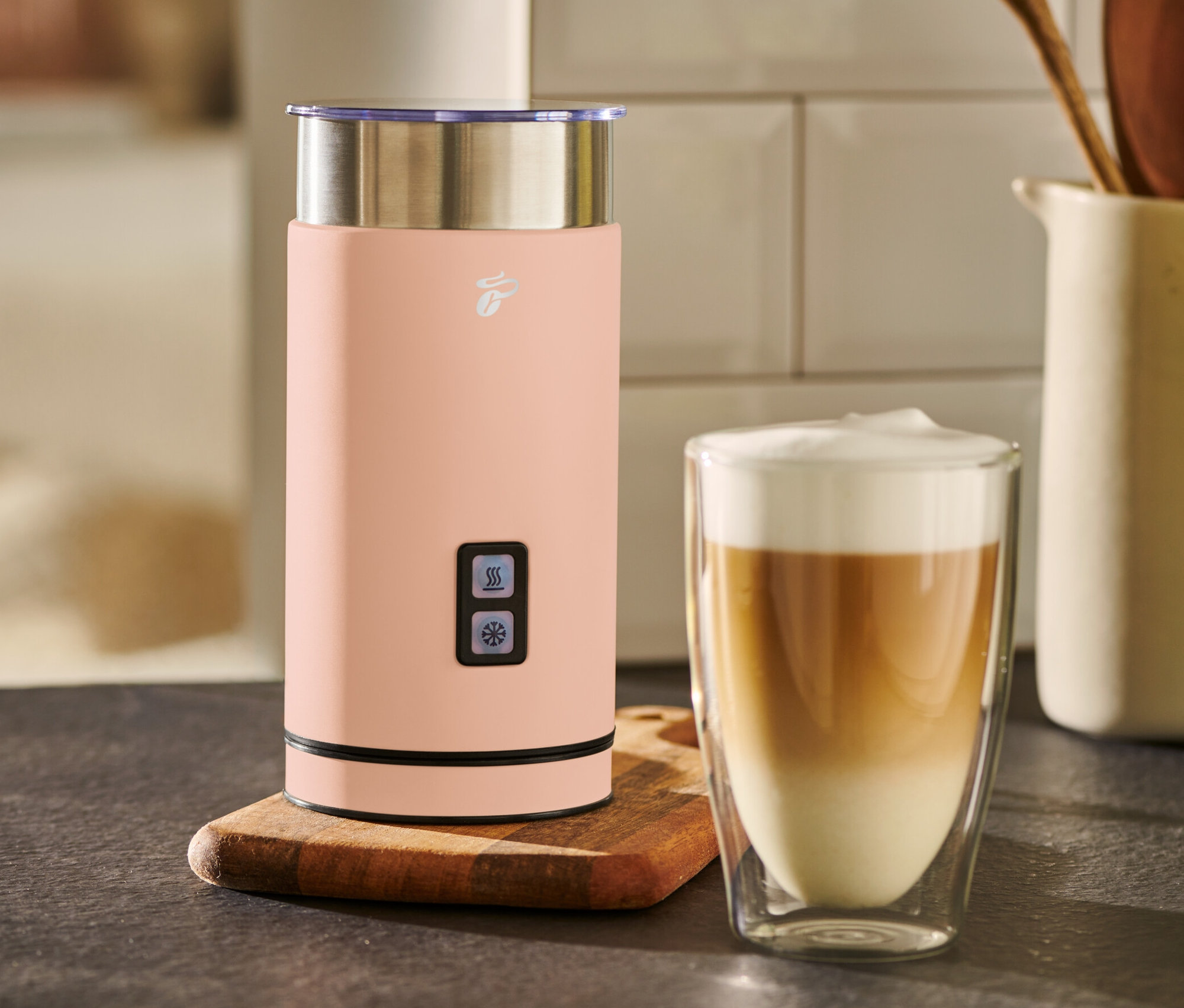 Meruňkový elektrický napěňovač mléka stojí vedle sklenice s kávou.