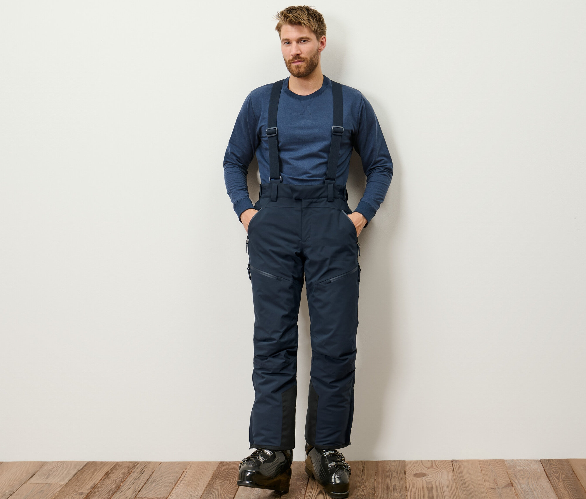 Muž stojí a má na sobě modré high-tech lyžařské kalhoty.