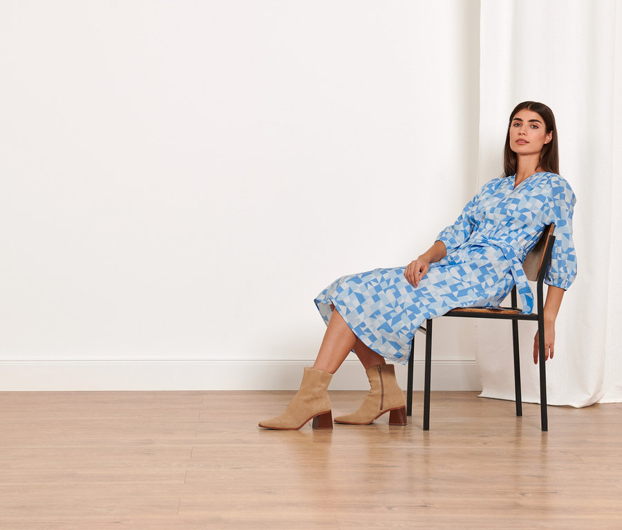 Žena sedí na židli a má na sobě tkané šaty s potiskem.