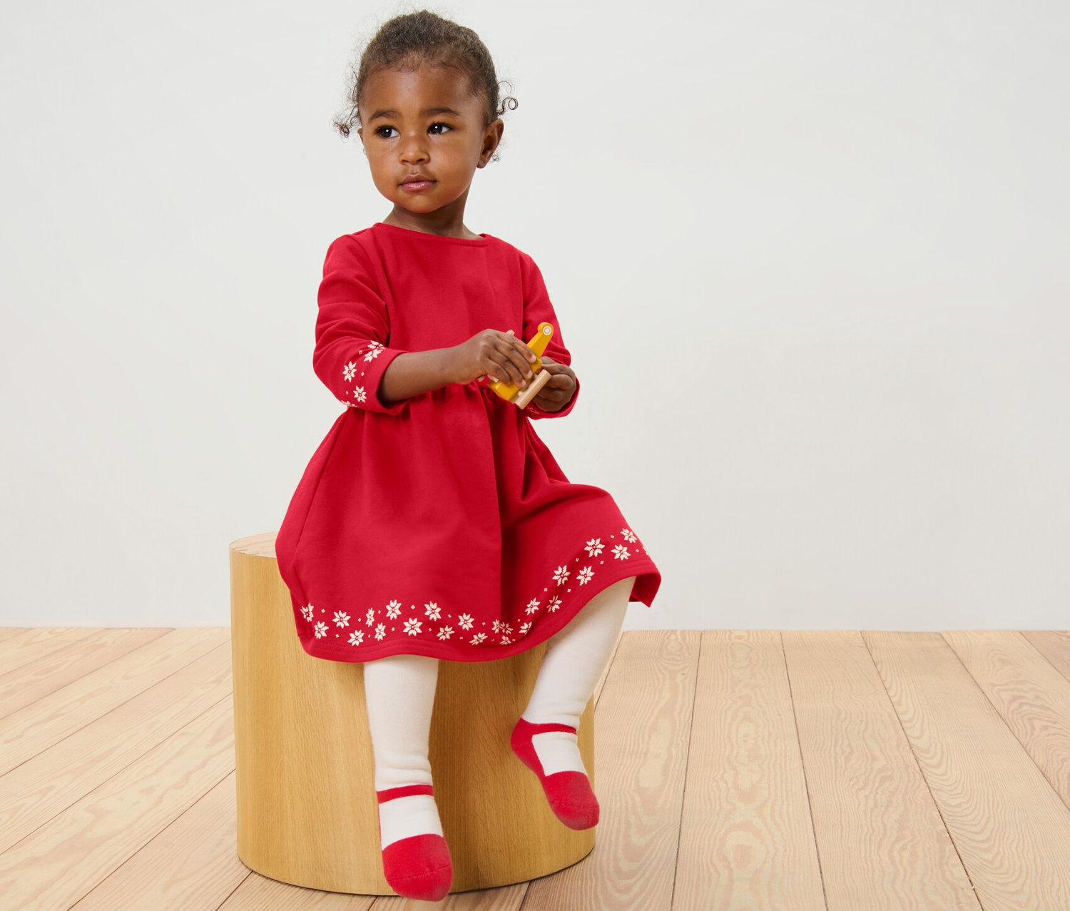 Holčička sedí na stoličce a má na sobě červené dívčí teplákové šaty s bílými květy.