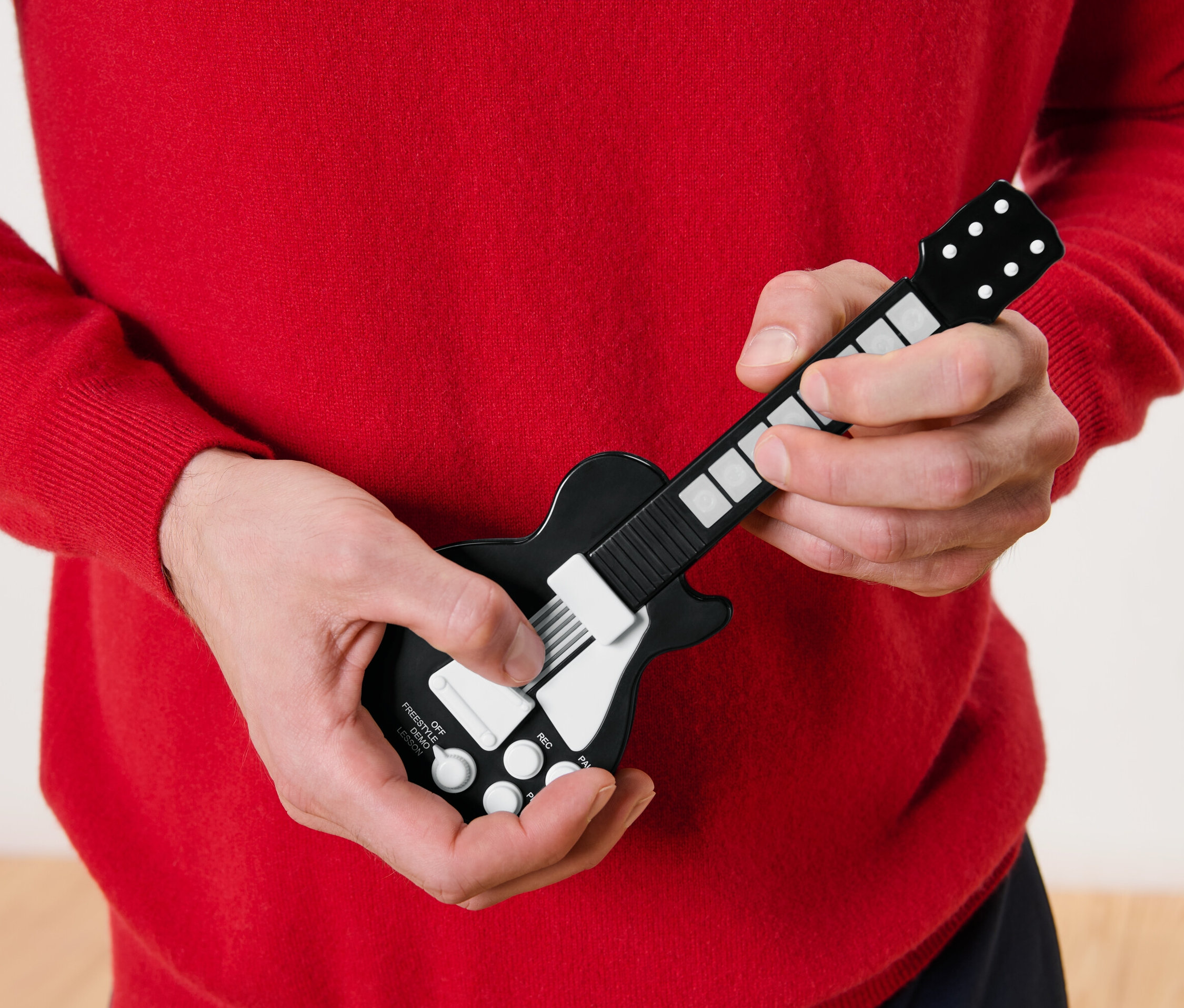 Muž v červeném svetru hraje na prstovou kytaru.
