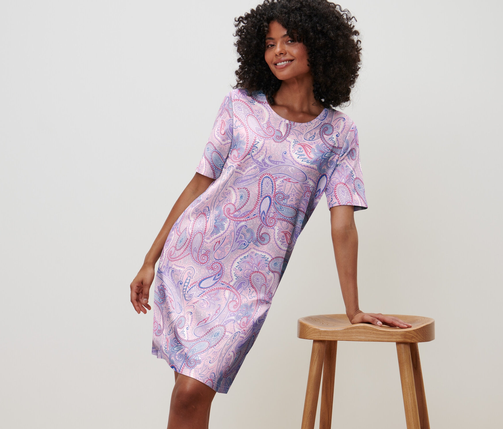 Žena opírající se o stoličku v noční košili s květinovým vzorem.