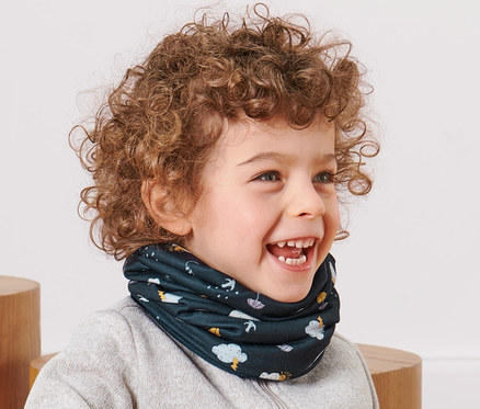 Usmívající se chlapeček s kudrnatými vlasy sedí a má na sobě dětský multifunkční šátek.