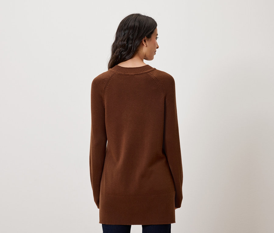 Zezadu je vidět žena s dlouhými tmavými vlasy v hnědém svetru s dlouhými rukávy.