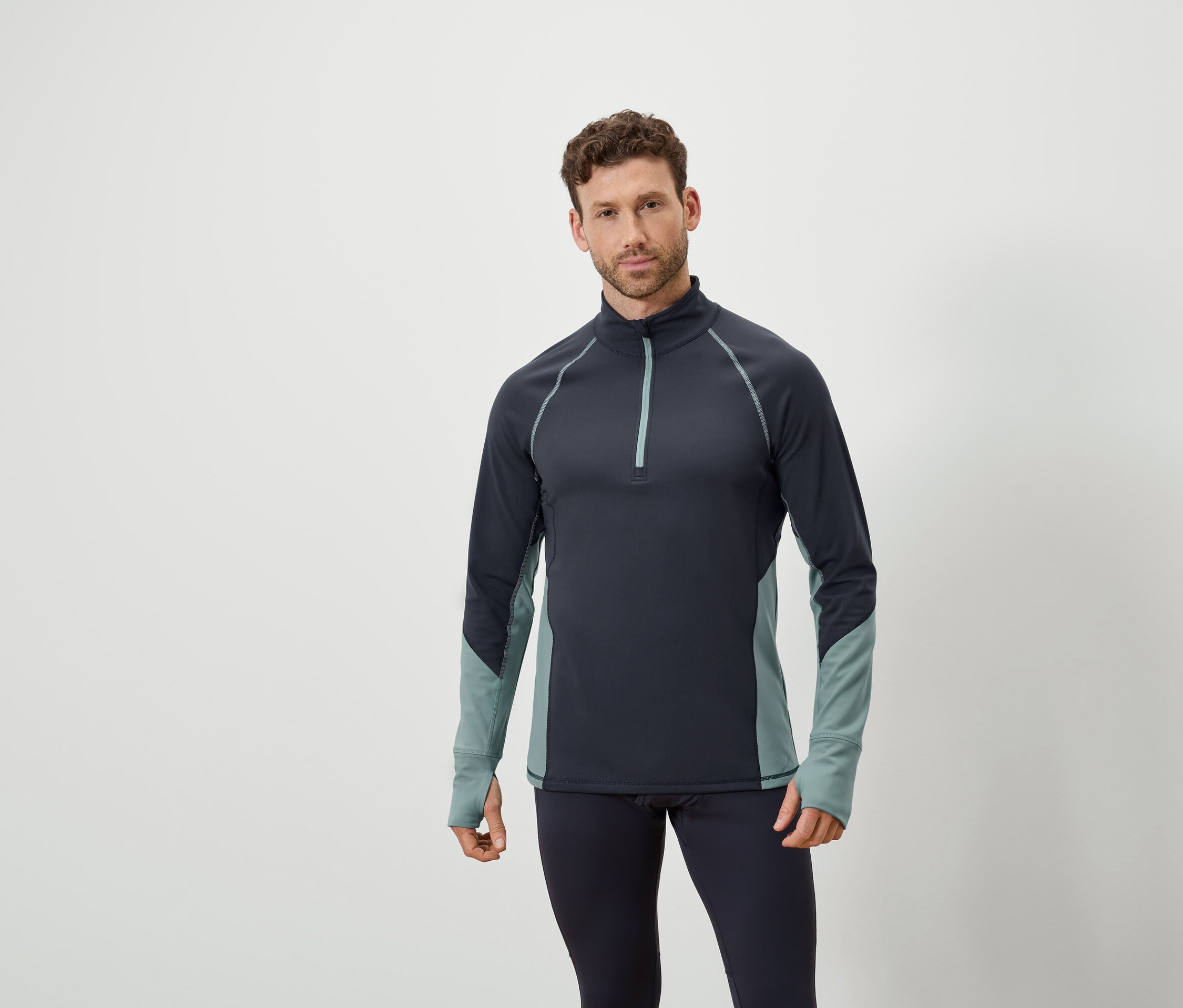 Muž pózuje v tmavě modrém topu s dlouhým rukávem a zipem a v tmavě modrých legínách.