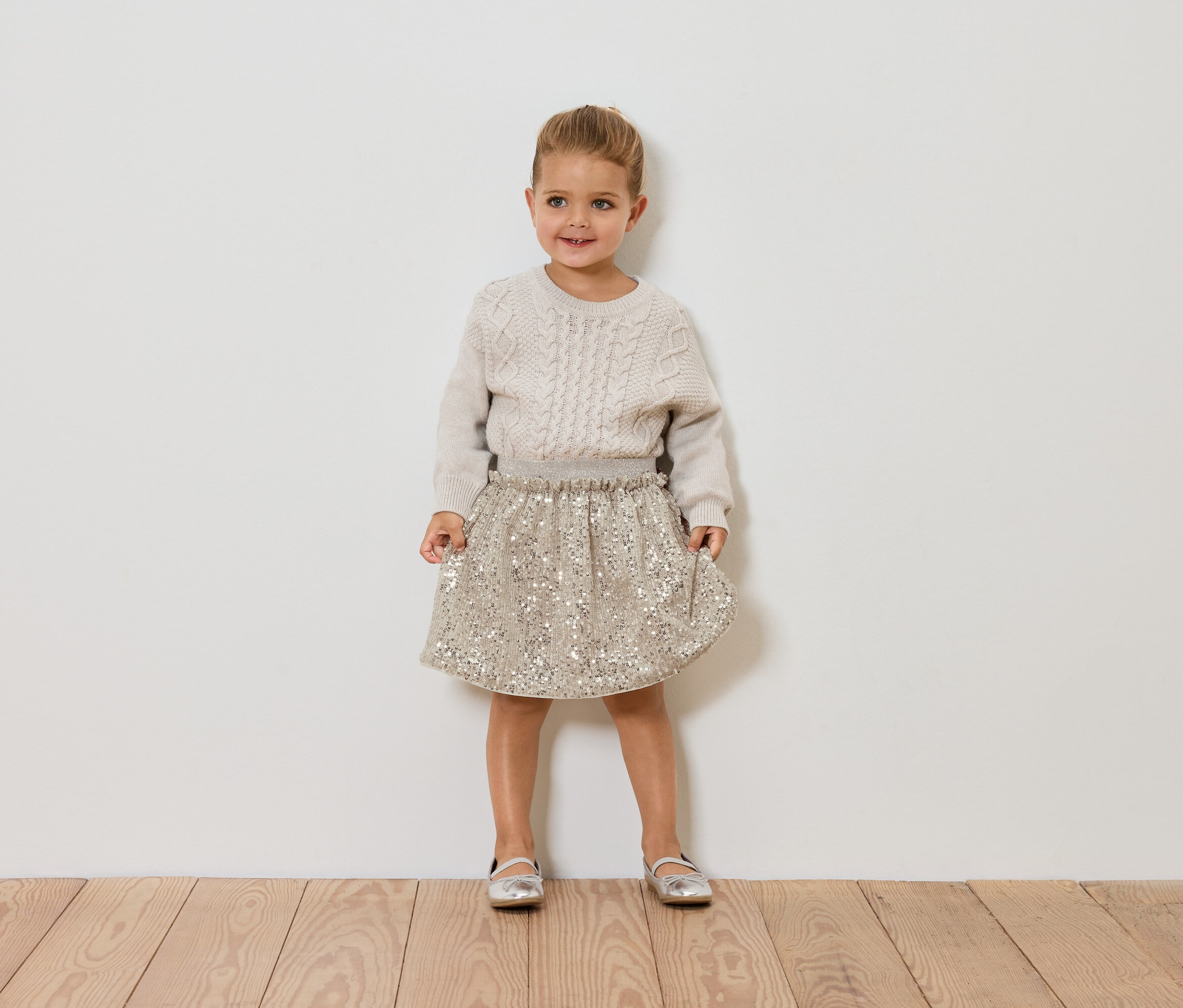 Dívka stojí a má na sobě svetr a sukni.