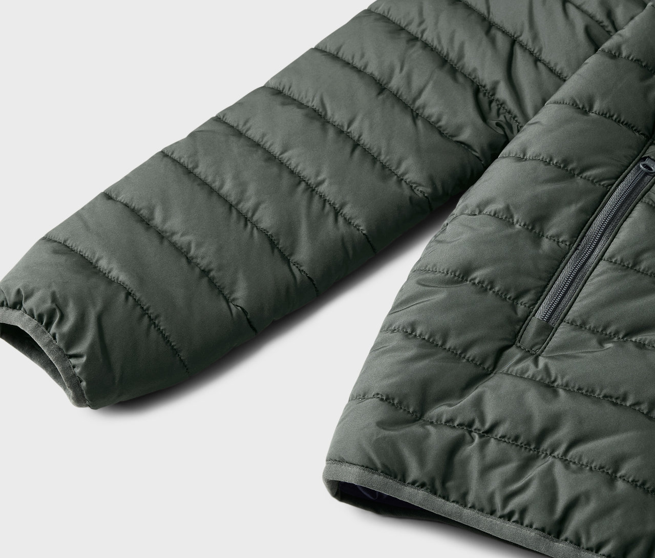 Detail dětské prošívané bundy, tmavě zelené barvy.