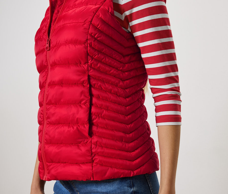 Částečný pohled na ženu v červené prošívané vestě a pruhovaném tričku.