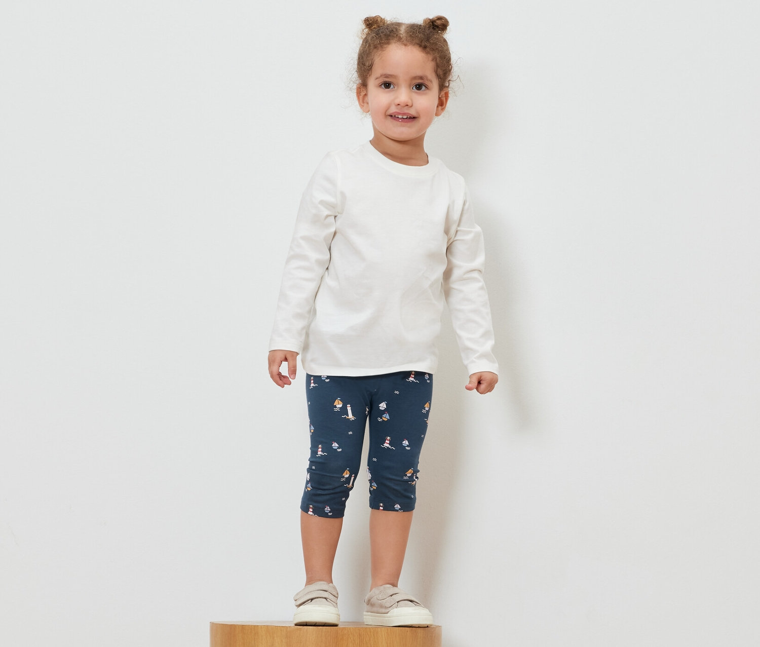 Dívka stojí na dřevěném podstavci a má na sobě námořnické 3/4 legíny.