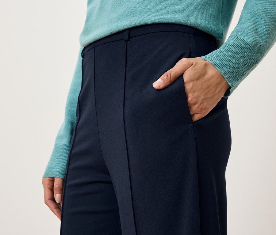 Detail dámských kalhot s rukou v kapse.