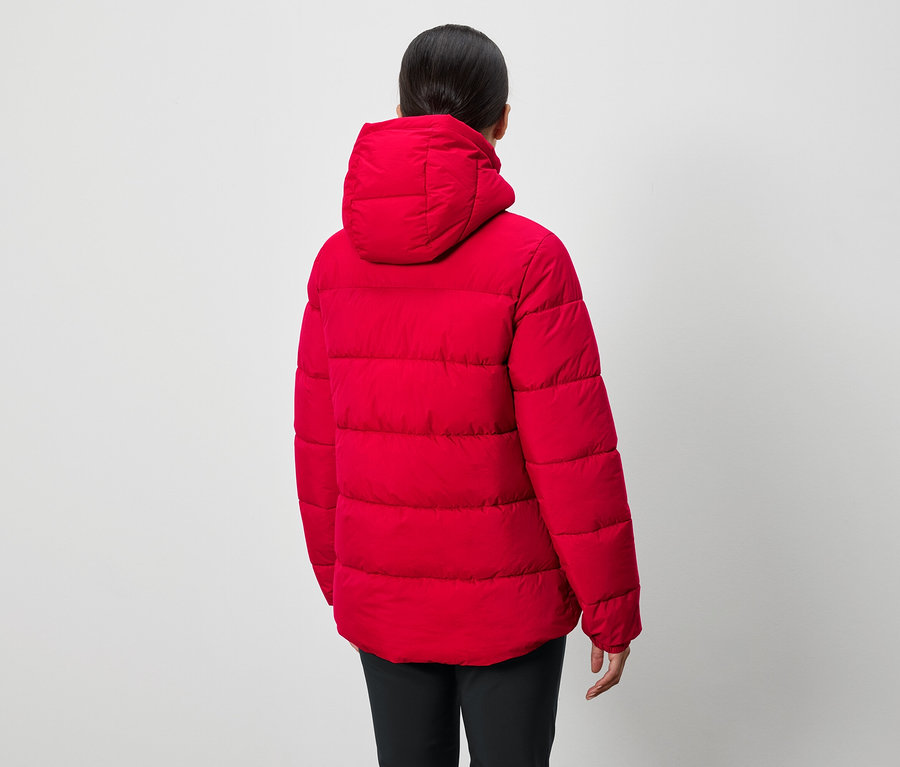 Osoba zády k fotoaparátu má na sobě červenou péřovou bundu s kapucí a černé kalhoty.