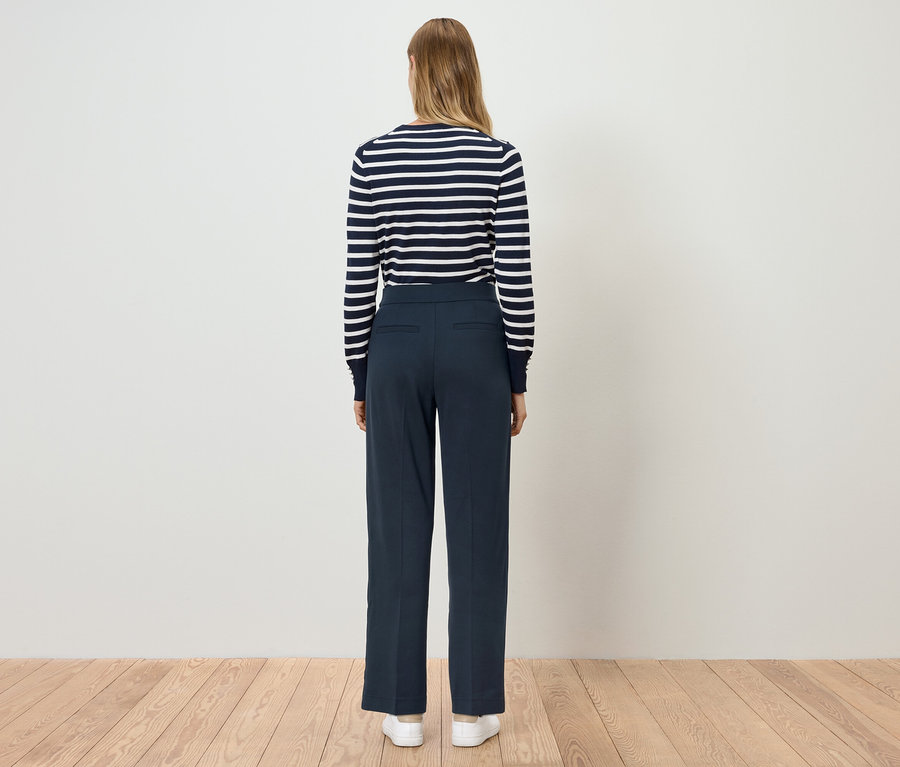 Žena stojí zády a má na sobě modré kalhoty a pruhovaný top.