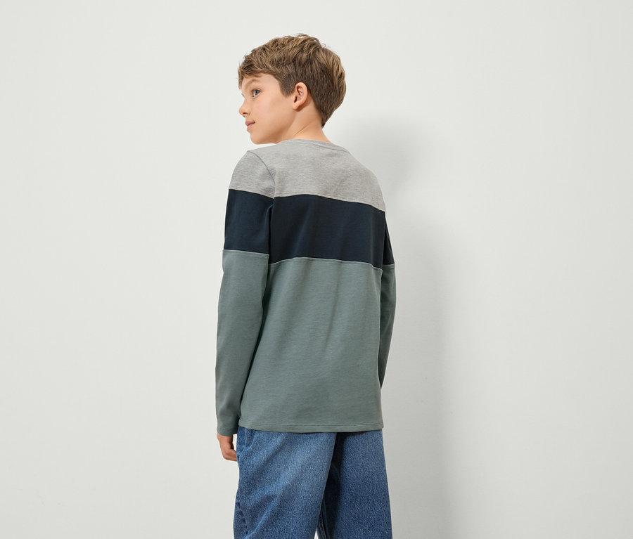 Chlapec v barevném tričku s dlouhým rukávem a džínových kalhotách stojí zády ke kameře.