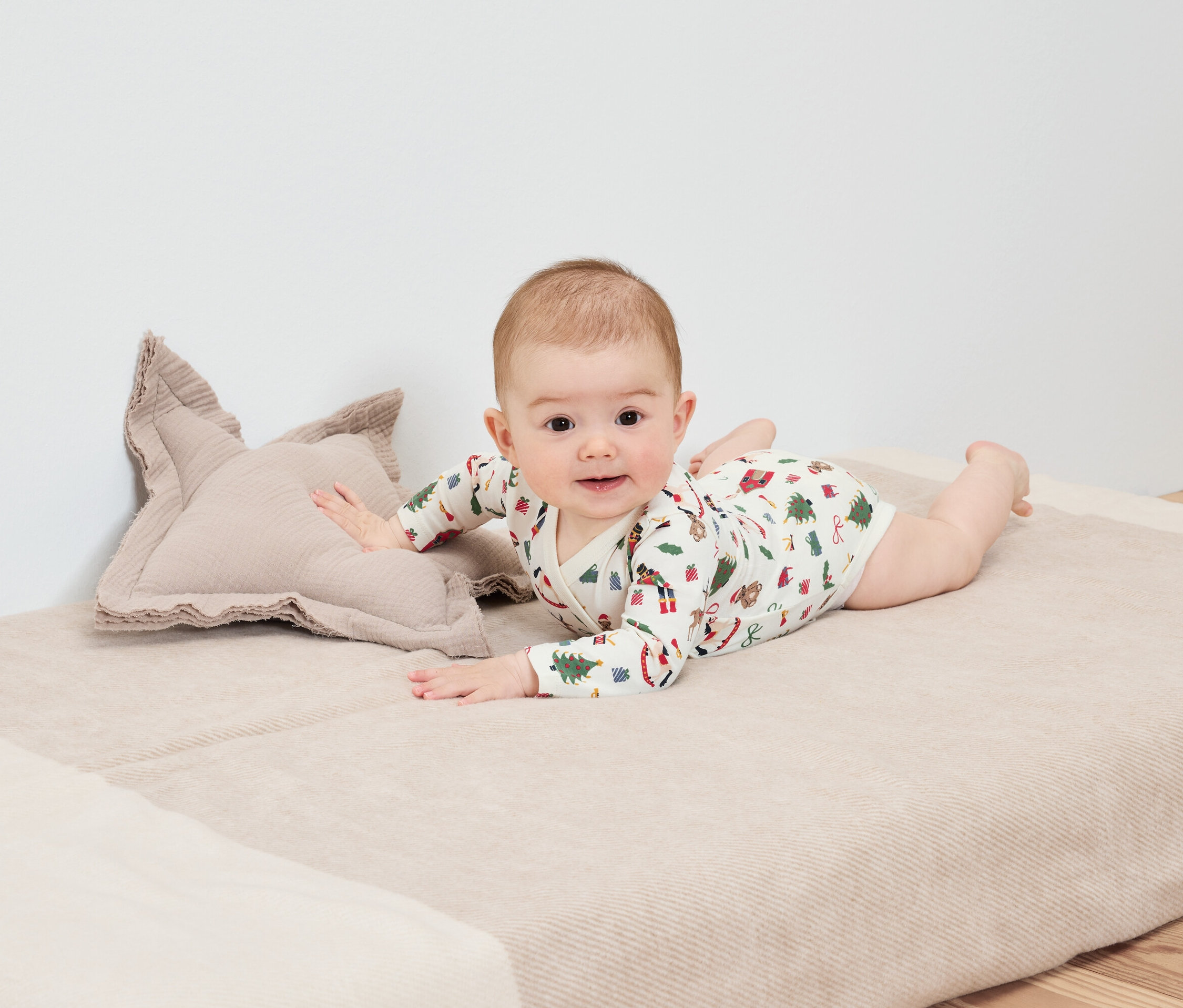 Dítě leží na břiše na dece vedle polštáře ve tvaru hvězdy.