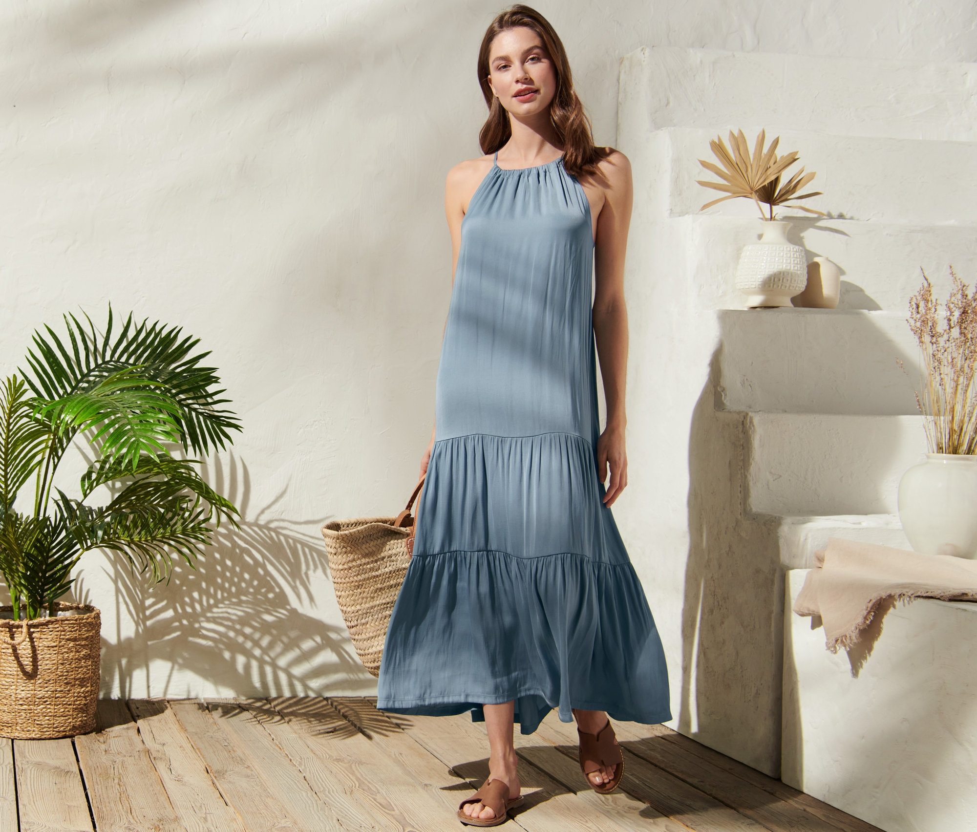 Žena pózuje venku v dlouhých šatech se zavazováním na šíji.