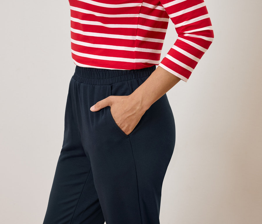 Žena s rukou v kapse tmavě modrých kalhot a červenobílém pruhovaném tričku.