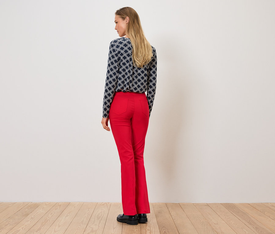 Žena stojí zády, má na sobě vzorovanou blůzu a červené kalhoty.