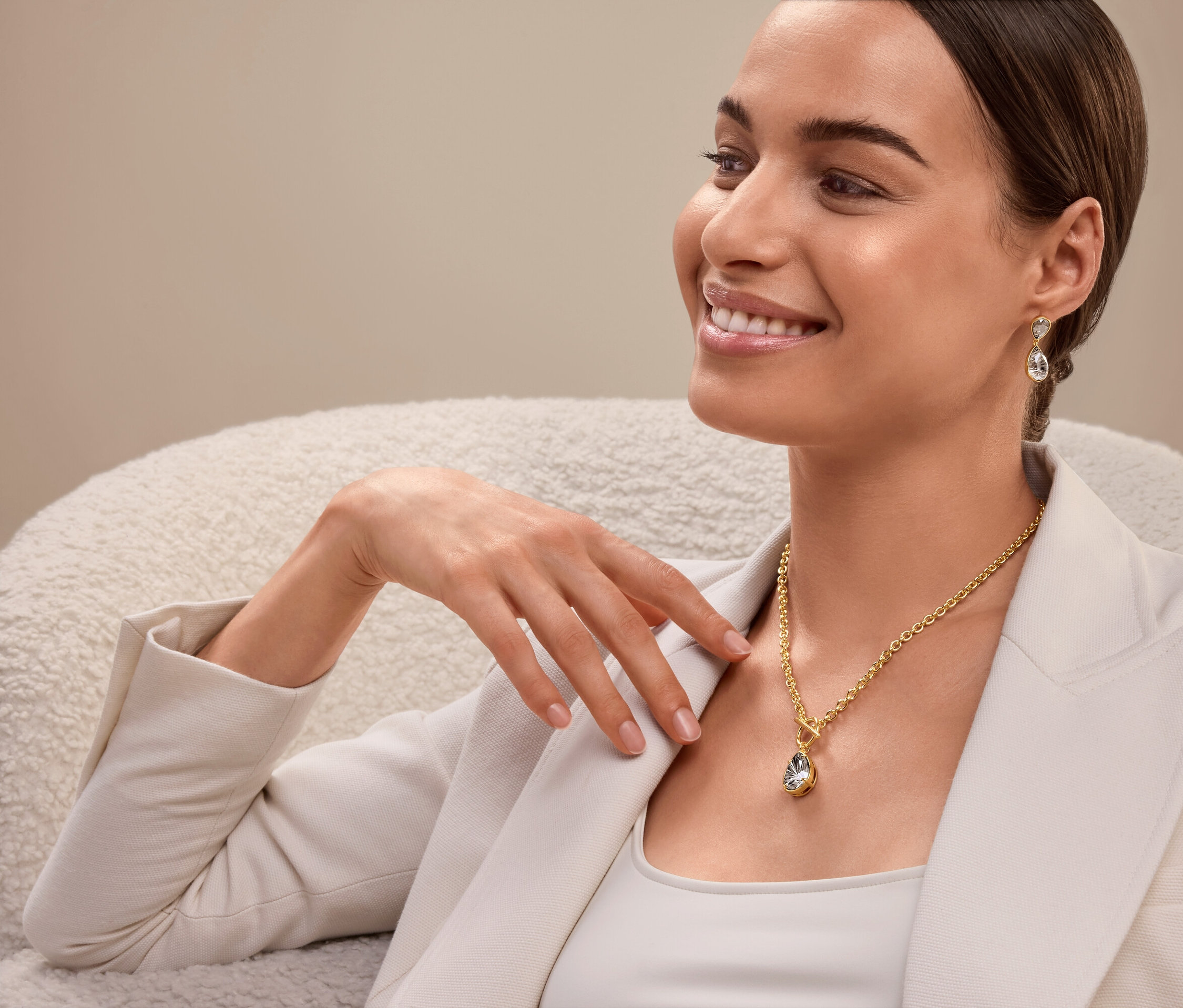 Žena sedí a má na sobě zlatý náhrdelník a náušnice.