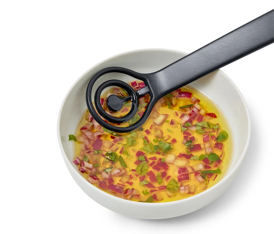 V bílé misce je vinaigrette s nasekanou červenou cibulí a bylinkami, míchaná černou metličkou.