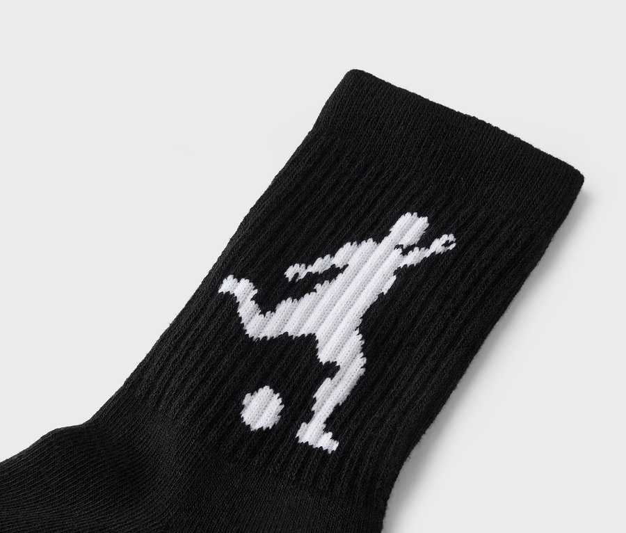 Detailní záběr černé ponožky s bílou siluetou fotbalisty kopajícího do míče.