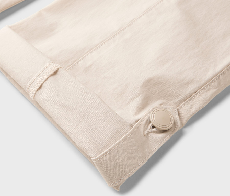 Detailní záběr na rukáv béžové košile, který je ohrnutý a zapnutý knoflíkem.