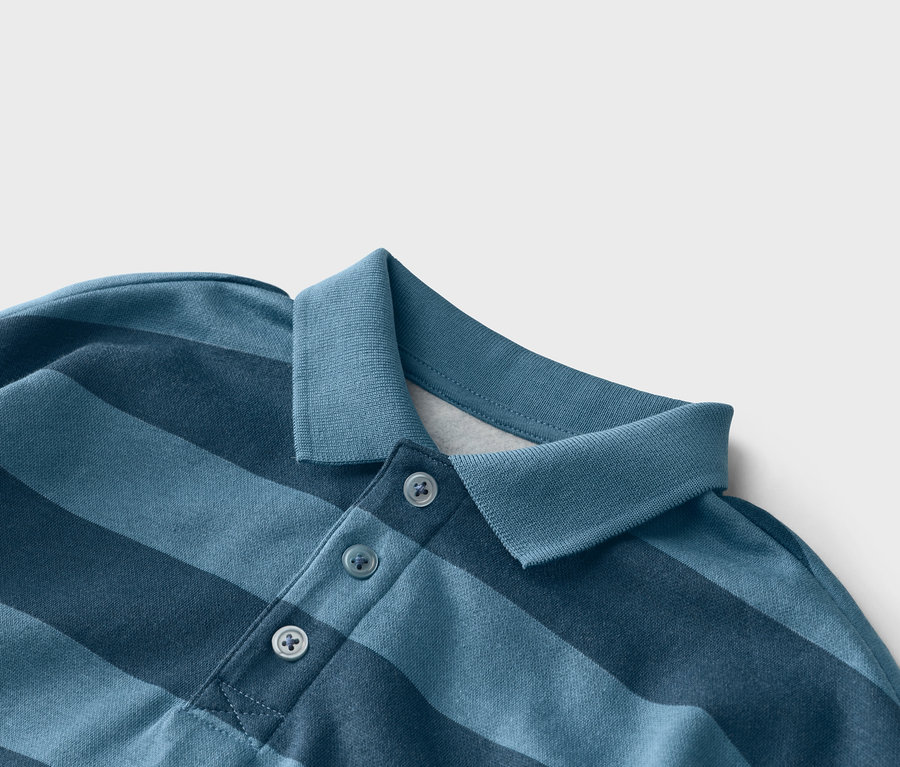 Detailní záběr na modré pruhované polo tričko se třemi knoflíky u límce.