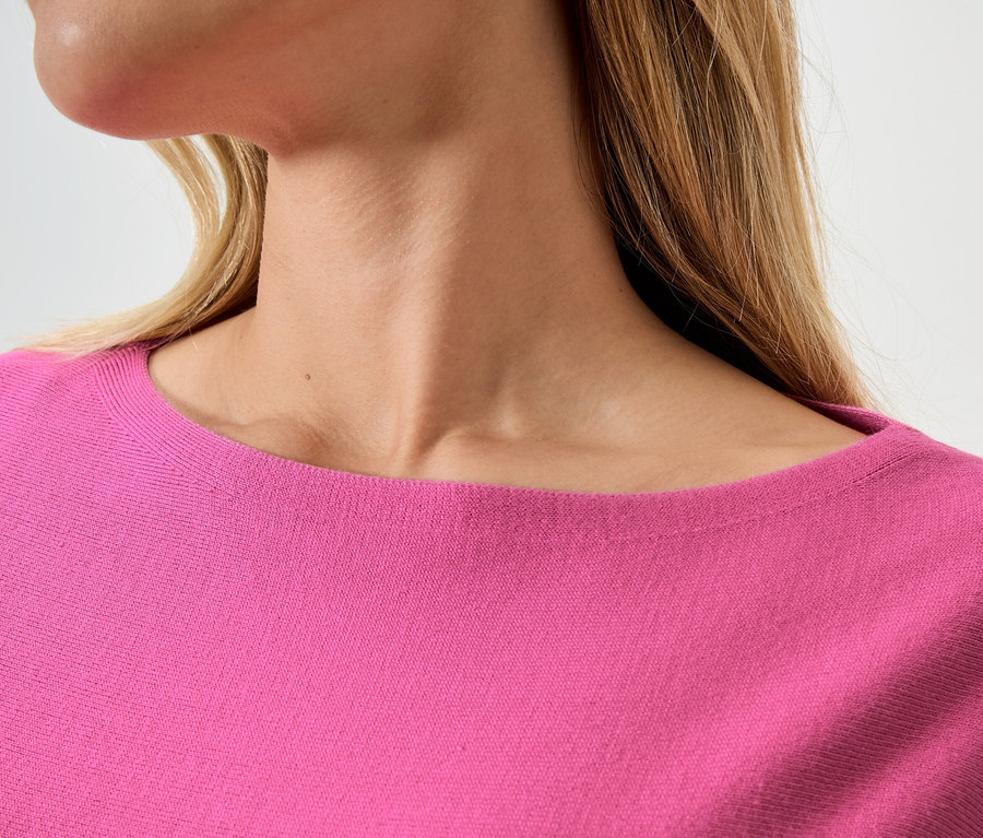 Detailní záběr ženy s blond vlasy v růžovém svetru.