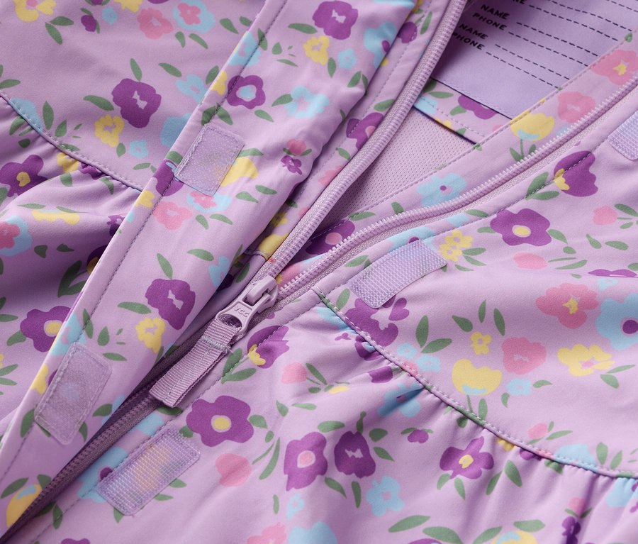 Detail fialové bundy s květinovým vzorem a zipem.