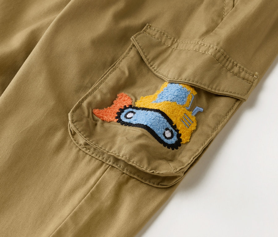 Detailní záběr khaki cargo kalhot s našitou kapsou zdobenou vyšívaným bagrem v oranžové, žluté a modré barvě.
