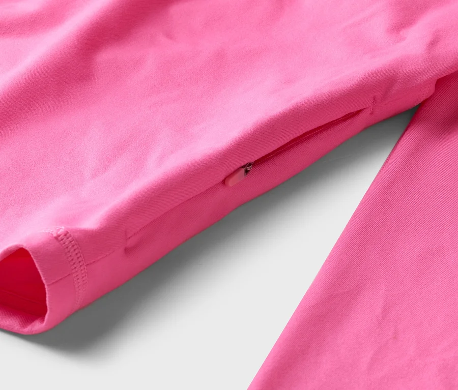 Detail růžového trička s dlouhým rukávem a kapsou na zip na rukávu.