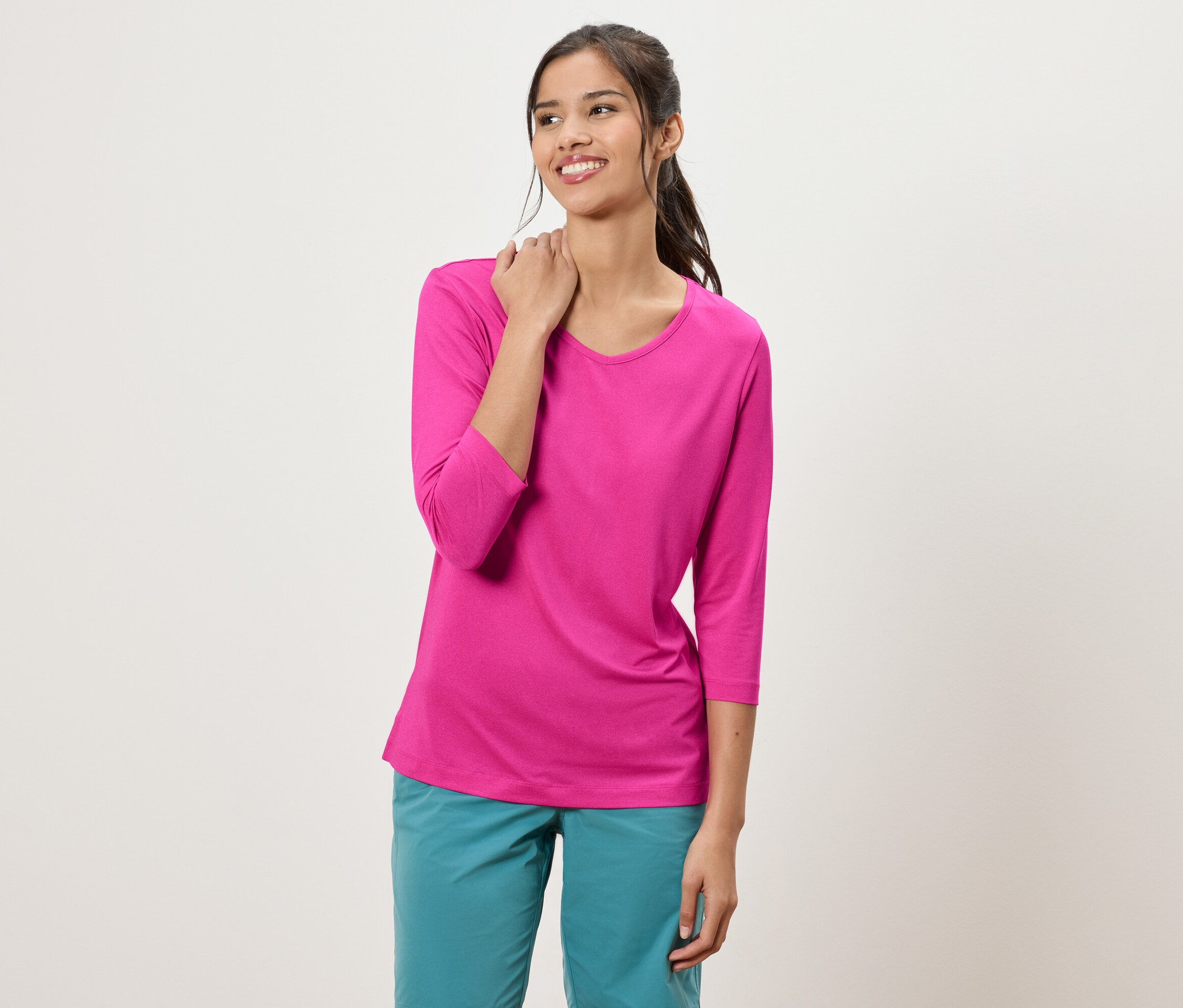 Žena s culíkem má na sobě růžový top s tříčtvrtečními rukávy a tyrkysové kalhoty.