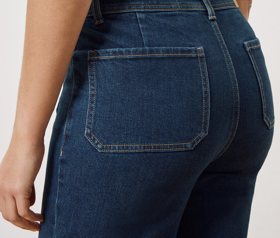 Detailní záběr na zadní část osoby v tmavě modrých džínách s našitými zadními kapsami.