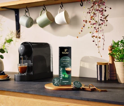 Černý kávovar připravuje kávu do sklenice vedle balení kapslí Espresso Brasil – 10 kapslí.