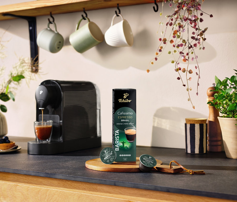 Černý kávovar připravuje kávu do sklenice vedle balení kapslí Espresso Brasil – 10 kapslí.