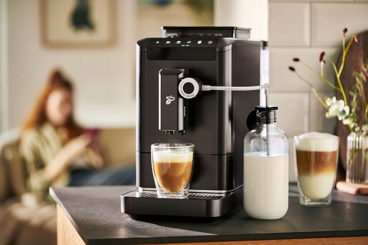 Automatický kávovar »Esperto 2 Milk« Granite Black připravuje kávu do sklenice. Vedle stojí karafa na mléko.
