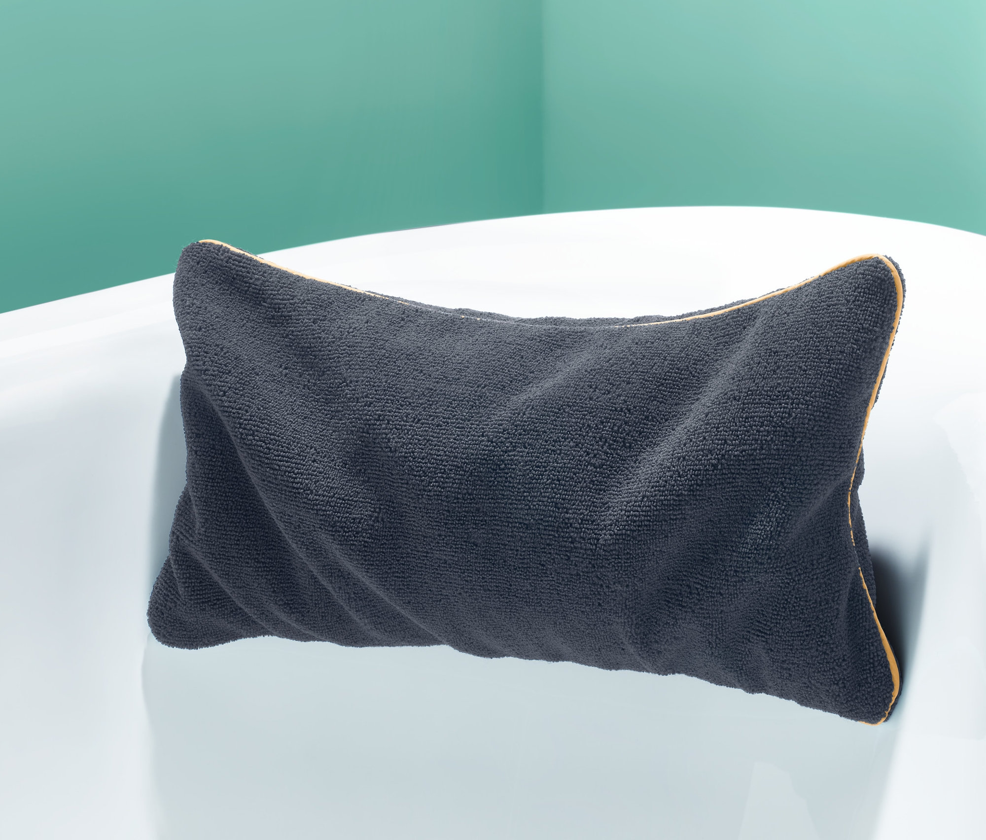 Antracitový polštářek do vany leží na okraji bílé vany.