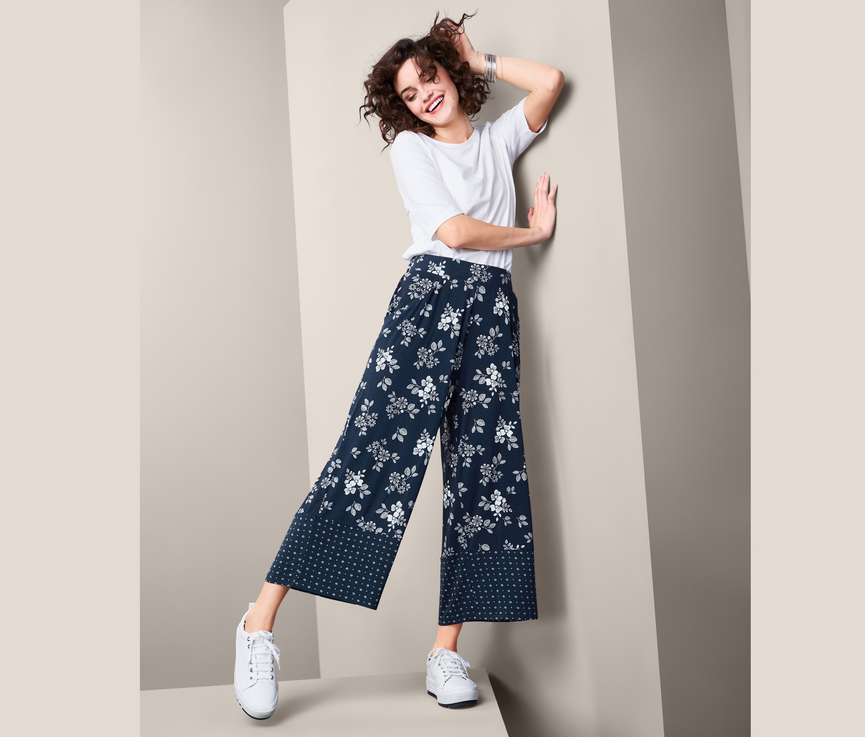 Žena pózuje v palácových kalhotách s potiskem a bílém tričku.