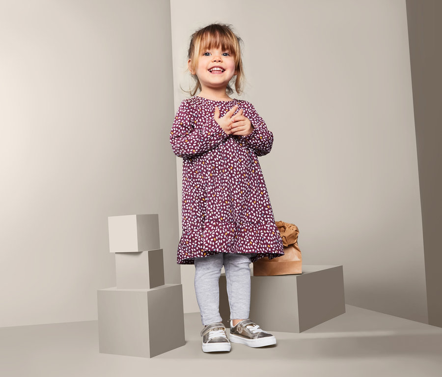 Usmívající se holčička stojí a má na sobě džínové šaty.