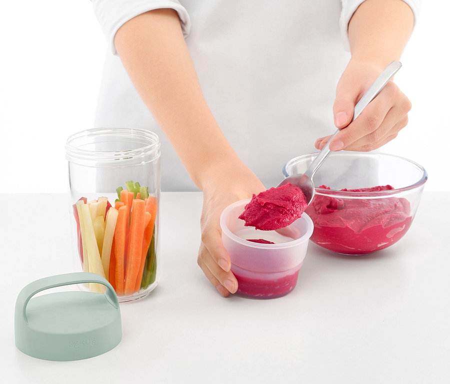 Žena lžící přendává červenou řepu z mísy do cestovní dózy na oběd. Vedle je sklenice se zeleninou a víko.