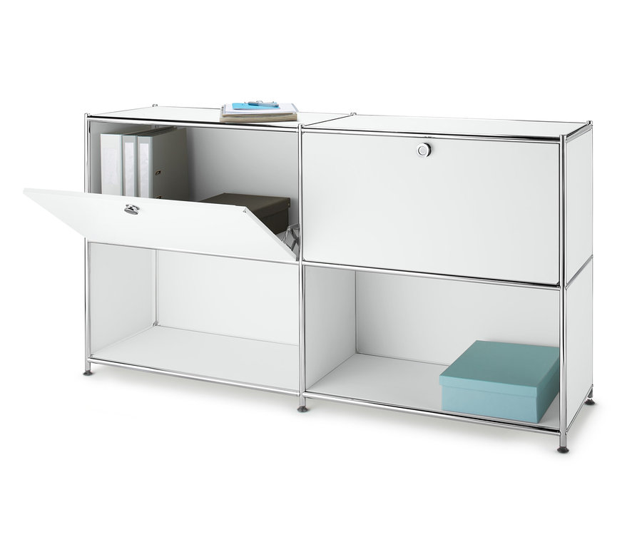 Bílá kovová odkládací skříňka se 2 přemístitelnými výklopnými dvířky, jedny dvířka jsou otevřené.