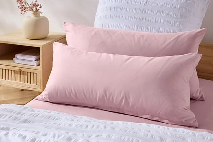Dva růžové povlaky na polštáře z mikrovlákna (cca 80 x 40 cm) na posteli s bílým přehozem.
