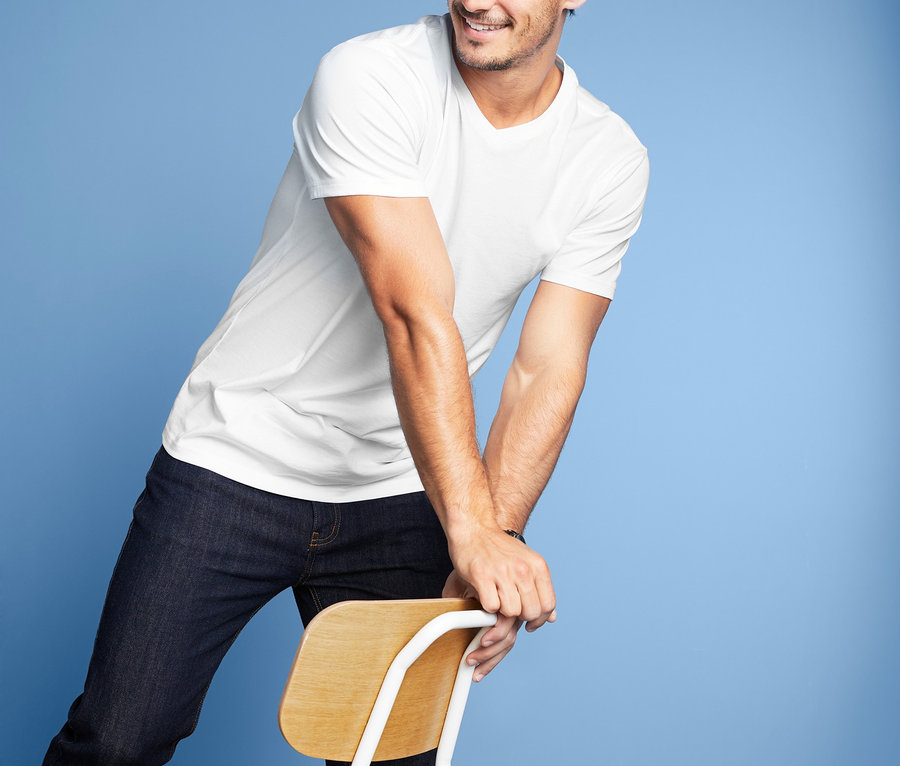 Muž se usmívá a opírá se o židli. Má na sobě bílé tričko s výstřihem do V ze sady po dvou.
