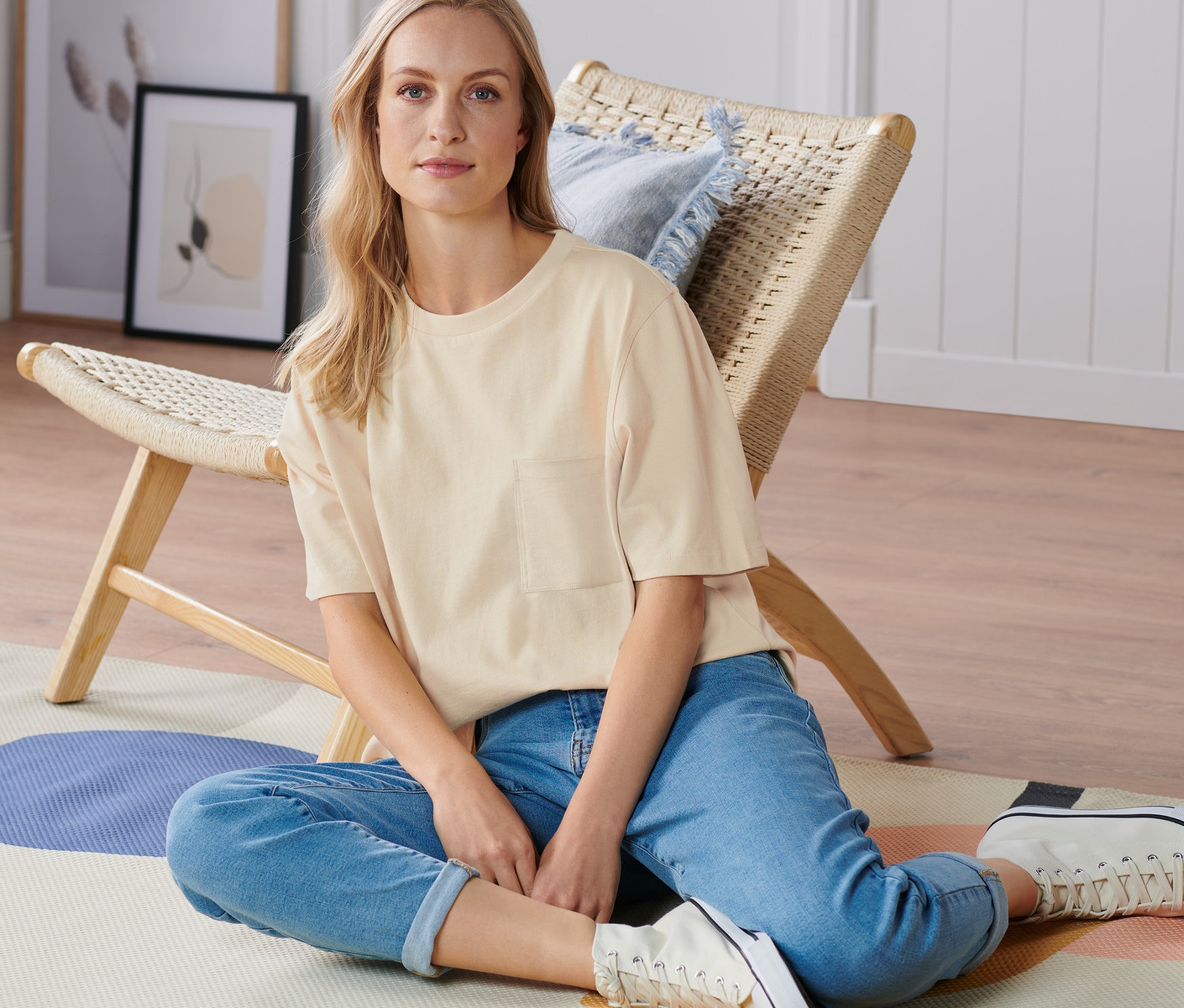 Žena sedí na podlaze a má na sobě pískové triko ve stylu oversized.