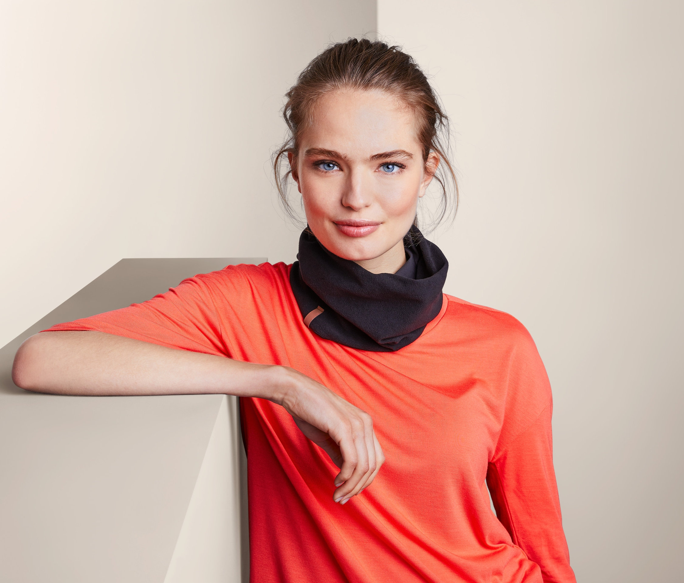 Žena opřená o zeď má na sobě multifunkční šálu a čepici.