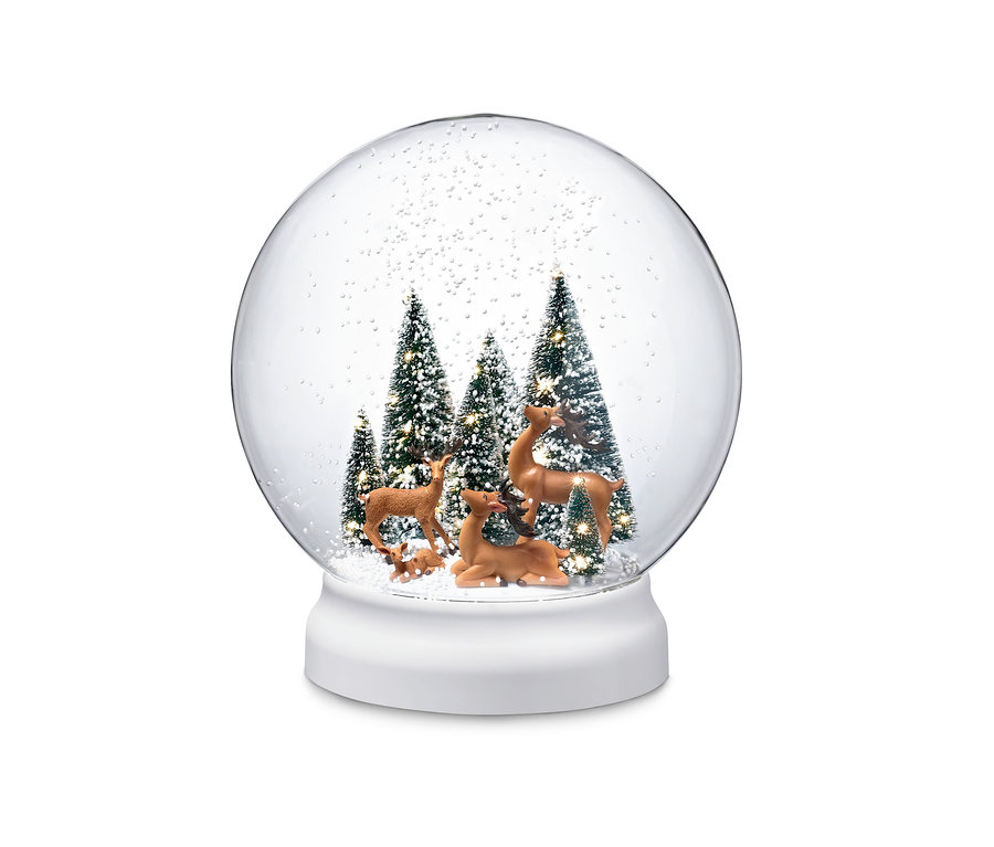 Uvnitř LED sněžítka stojí figurky jelena mezi zasněženými stromy.