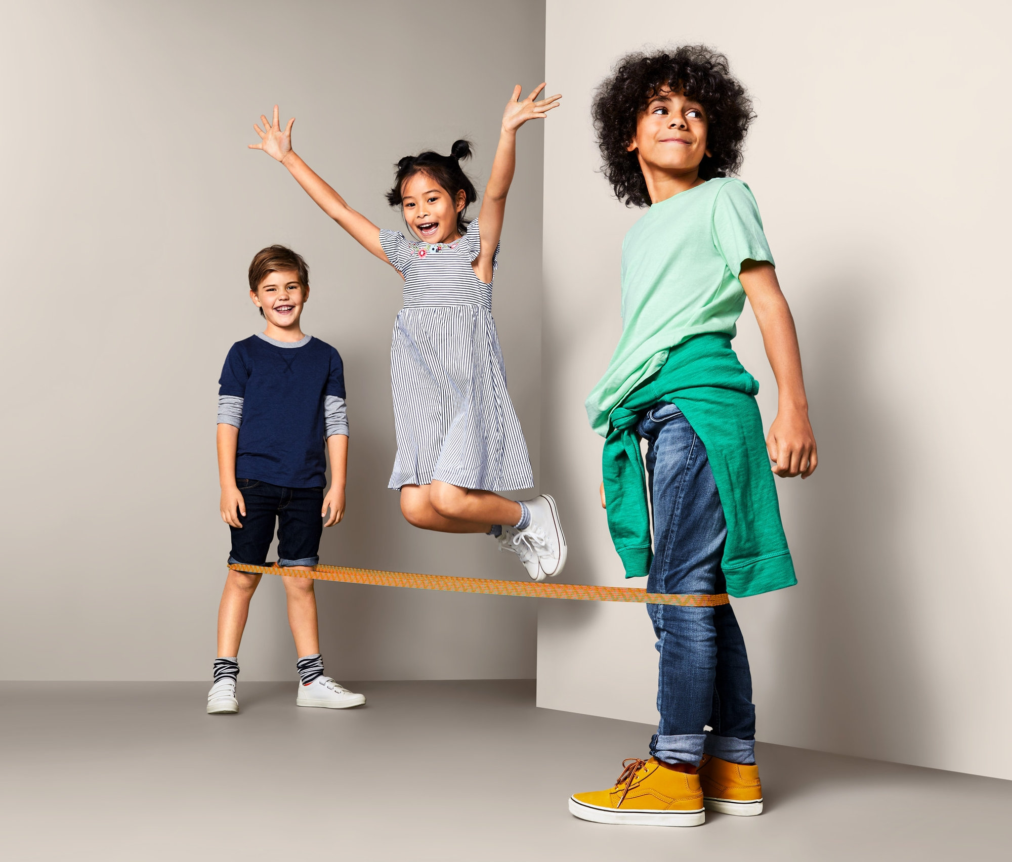 Tři děti si hrají se skákací gumou. Dívka skáče přes gumu, zatímco ji drží dva chlapci.