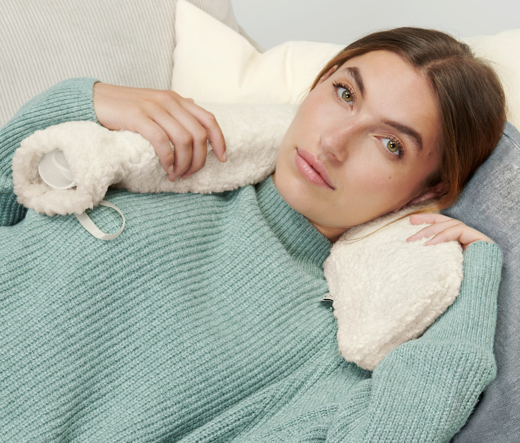 Žena leží na gauči a drží podlouhlý termofor.