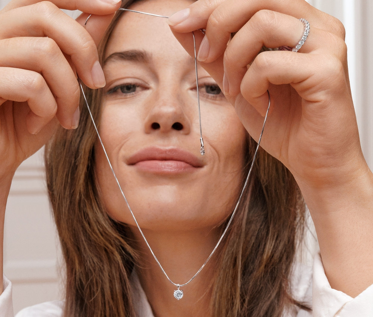 Žena drží řetízek s přívěskem se solitérním zirkonem. Na prsteníčku má prsten Memoire, rhodiované stříbro 925/1000, se zirkony.