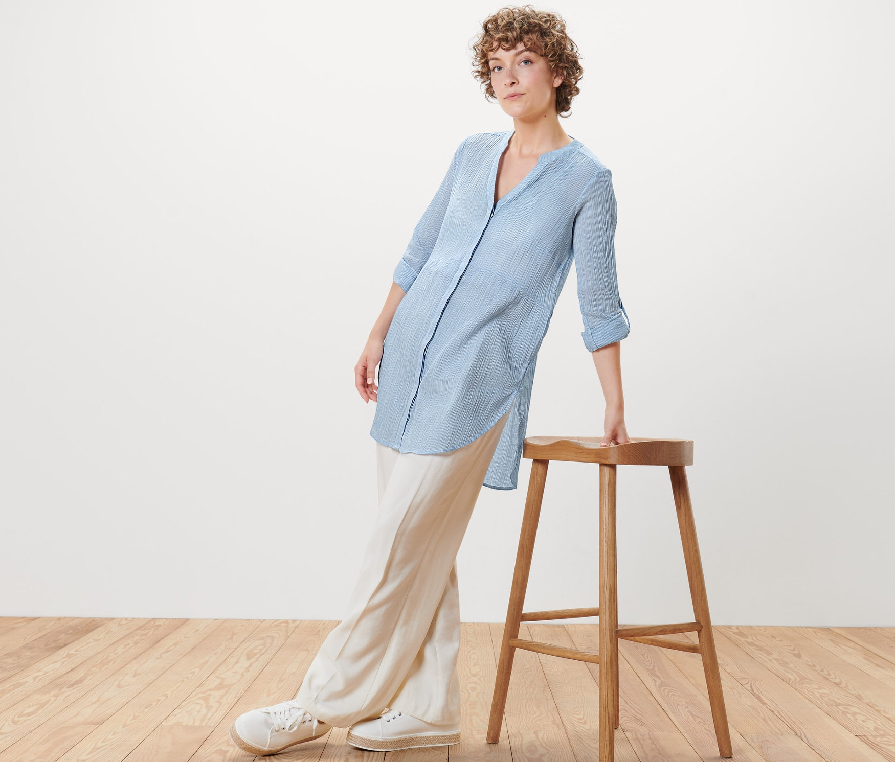 Žena opřená o dřevěnou stoličku má na sobě dlouhou proužkovanou halenku.