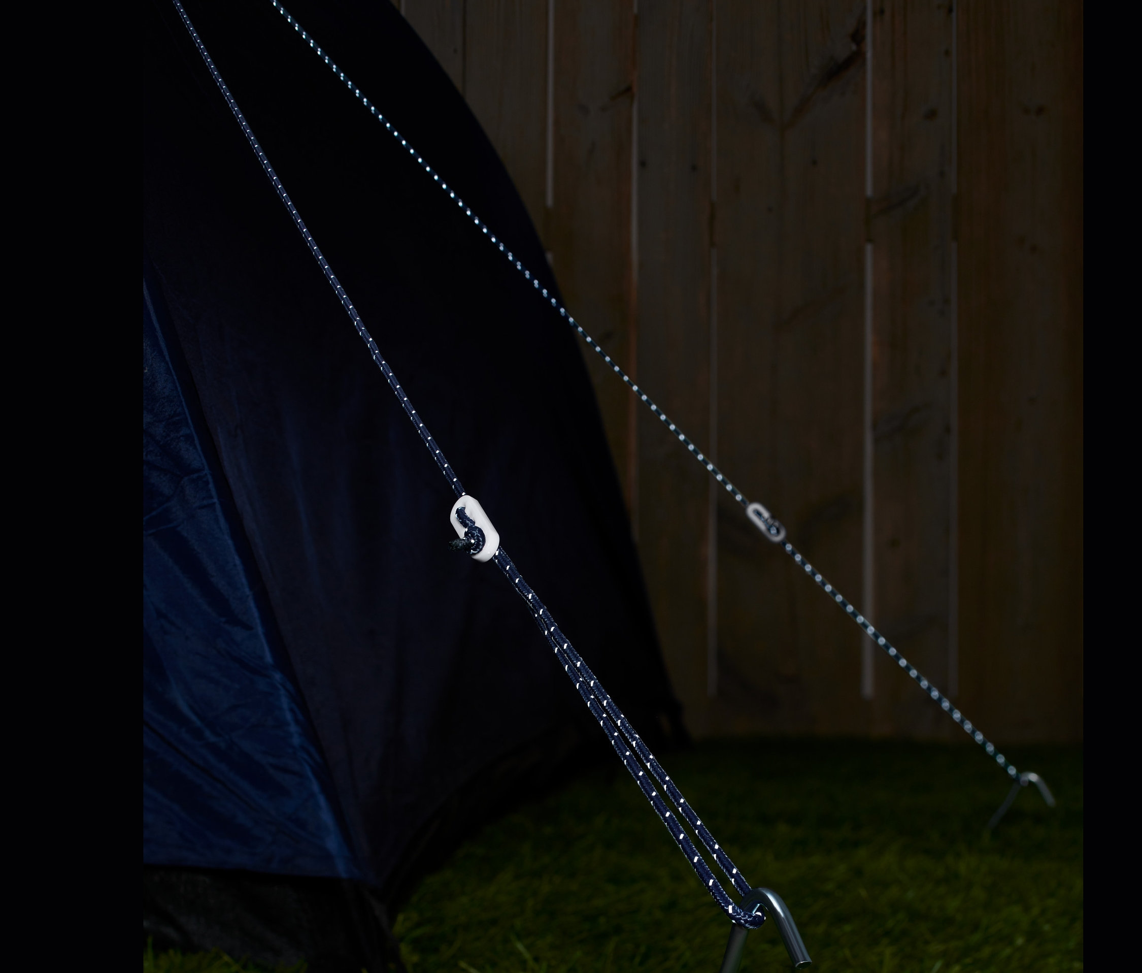 Dva reflexní napínací lana jsou připevněna ke stanu a kolíku na trávě.